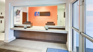 A reception area with a counter, a reception desk, and a large window. - Motel 6 Roanoke, TX - Northlake - Speedway (Roanoke)