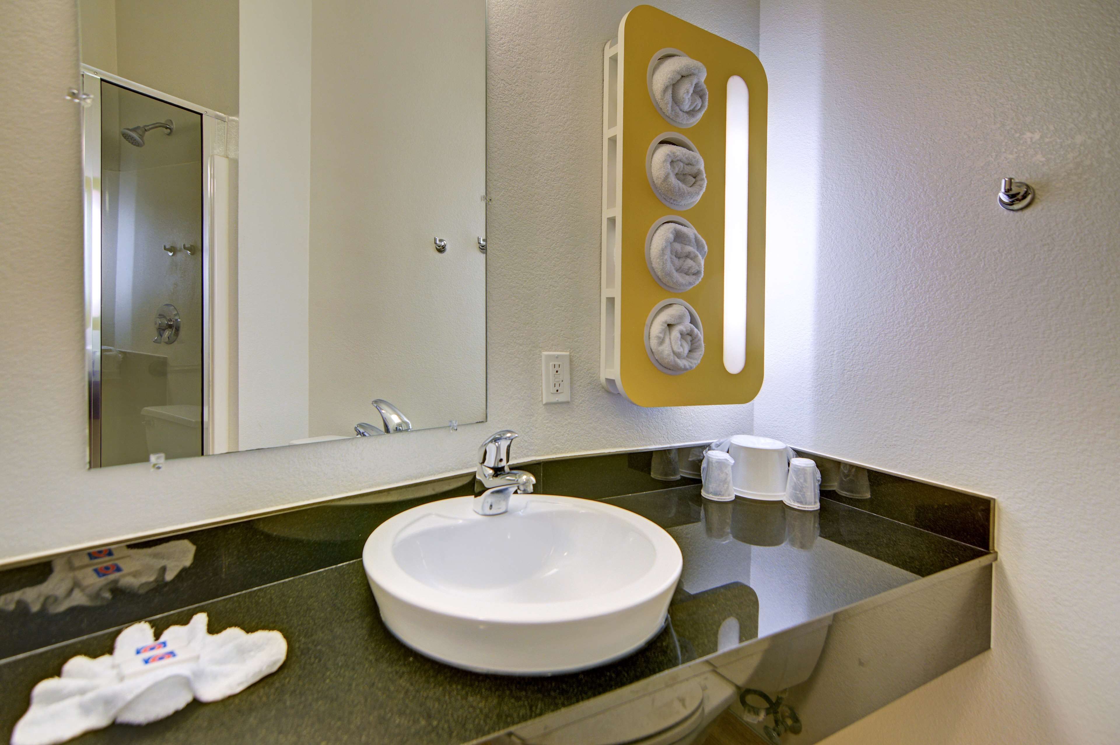 A bathroom with a white sink, a mirror, and a towel rack with four towels.