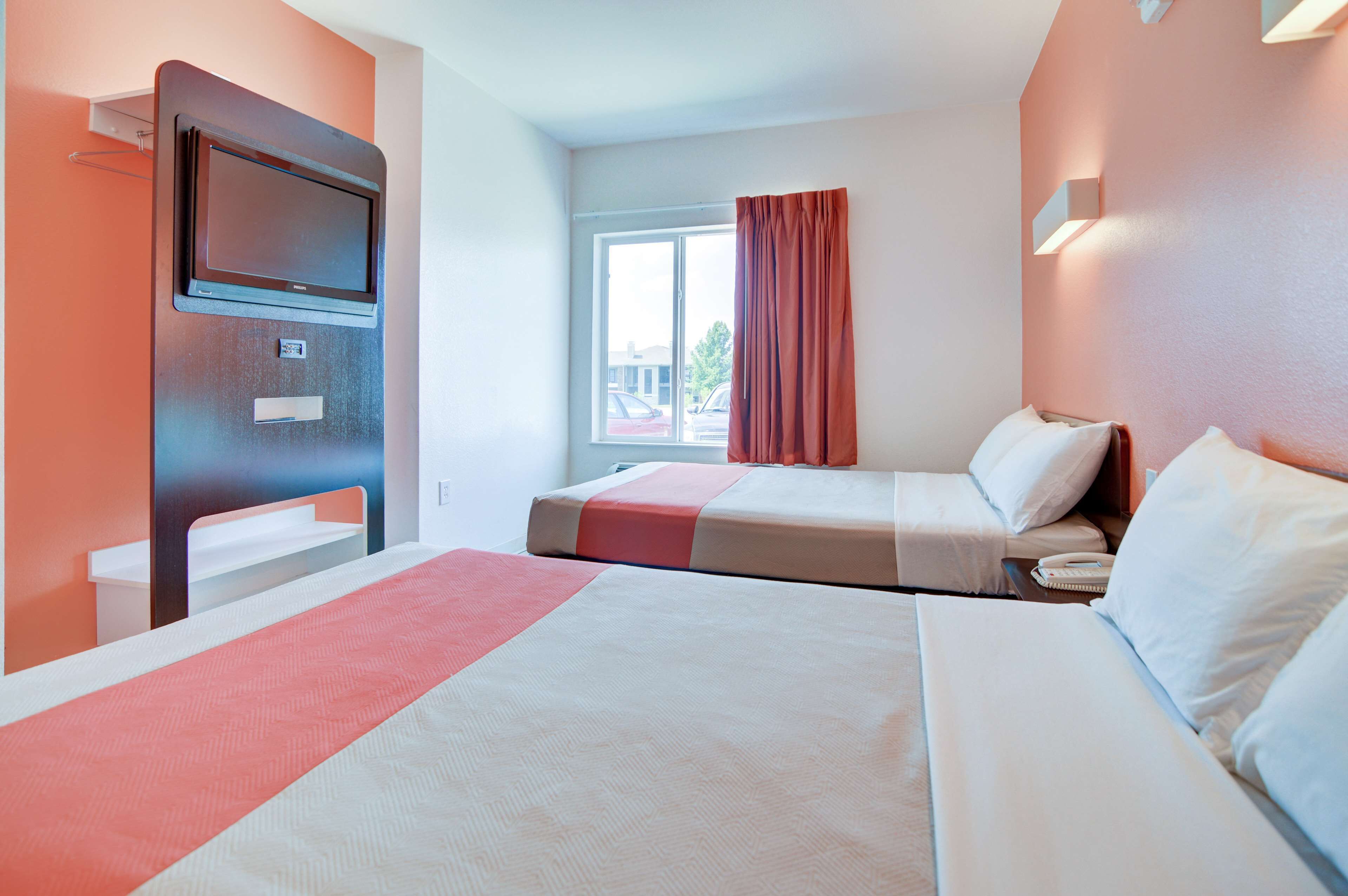 Een hotelkamer met twee bedden, een televisie, een raam met gordijnen en uitzicht op buiten.