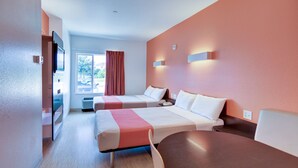 A hotel room with two beds, a dining table, a TV, and a window with curtains. - Motel 6 Roanoke, TX - Northlake - Speedway (Roanoke)