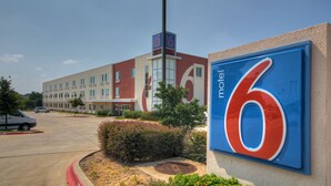 A motel with a large '6' sign, a parking lot, and a building with multiple windows. - Motel 6 Roanoke, TX - Northlake - Speedway (Roanoke)