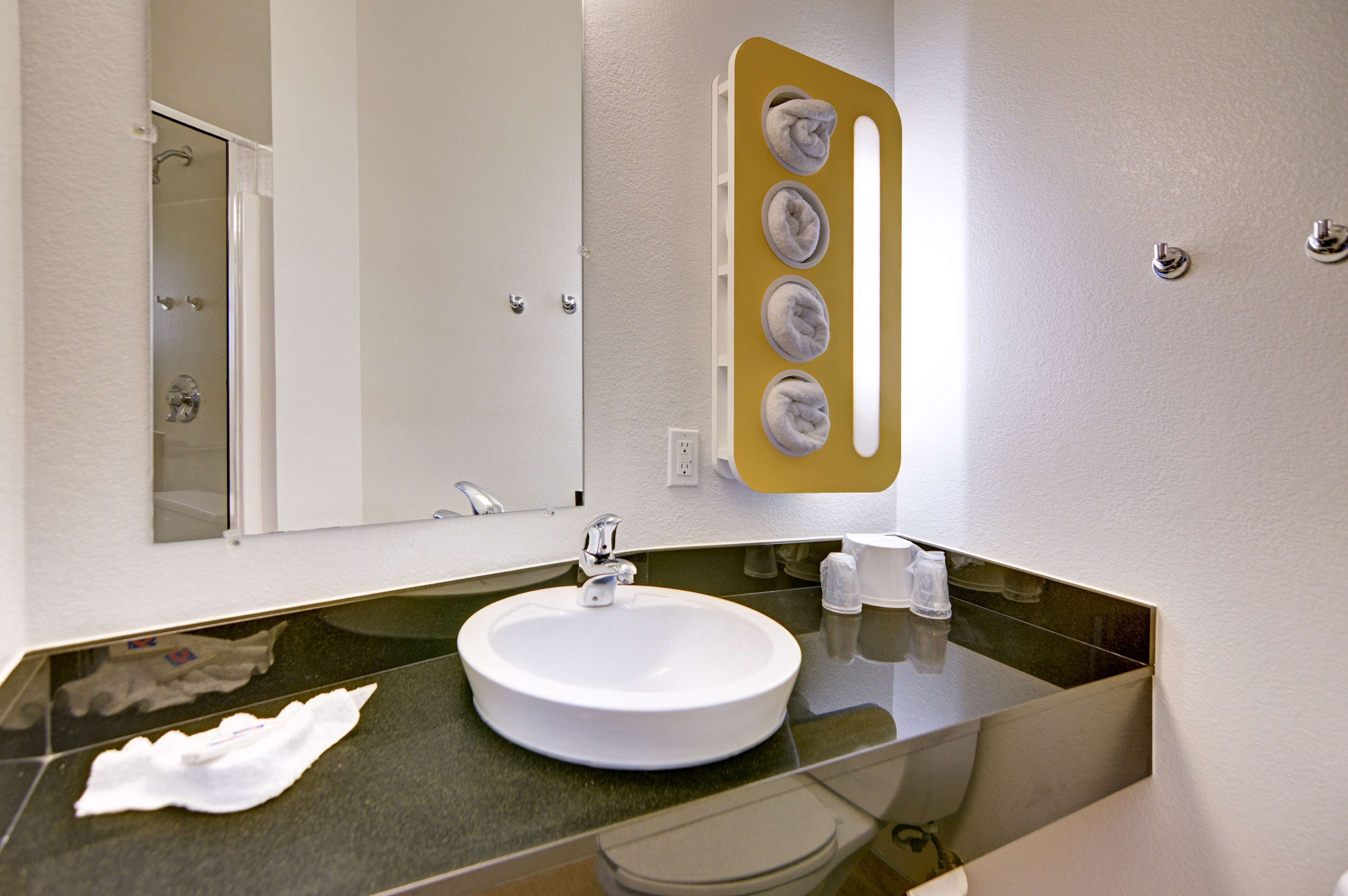 Une salle de bain moderne avec un lavabo rond blanc, un miroir et un porte-serviettes avec quatre serviettes.