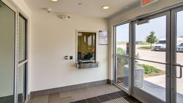 A clean, modern entrance with a glass door, a small reception desk, and a security camera on the ceiling.