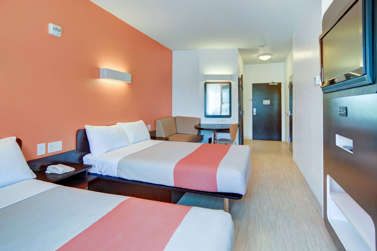 A hotel room with two beds, a desk, a chair, and a small table.