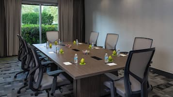 Ein Konferenzraum mit einem langen Tisch, Stühlen, Wasserflaschen und einer Obstschale.