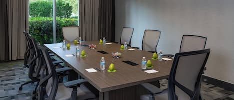 Ett konferensrum med ett långt bord, stolar, vattenflaskor och en skål med frukt.