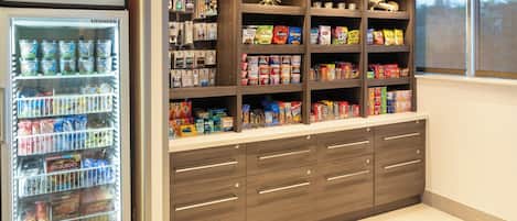 A kitchenette with a Liebherr refrigerator stocked with beverages, a variety of snacks, and a wooden cabinet with drawers.