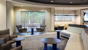Eine moderne Hotellobby mit Sitzgelegenheiten, darunter Sofas und Sessel, einem Couchtisch und einem Fernseher.