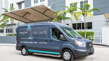 Un furgone blu con la scritta 'SPRINGHILL SUITES' e 'FEEL SUITE', parcheggiato di fronte a un edificio moderno con palme.