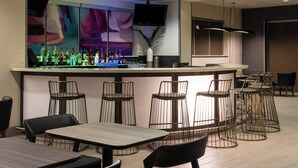 Eine Bar mit Theke, Hockern und einem Fernseher. Tische und Stühle stehen rund um die Bar.