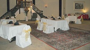 A formal dining room with round tables, white tablecloths, and chairs with yellow sashes. - The George Washington Hotel (Washington)