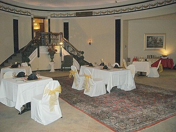 Une salle à manger élégante, avec des tables rondes, des nappes blanches et des chaises ornées de rubans jaunes.