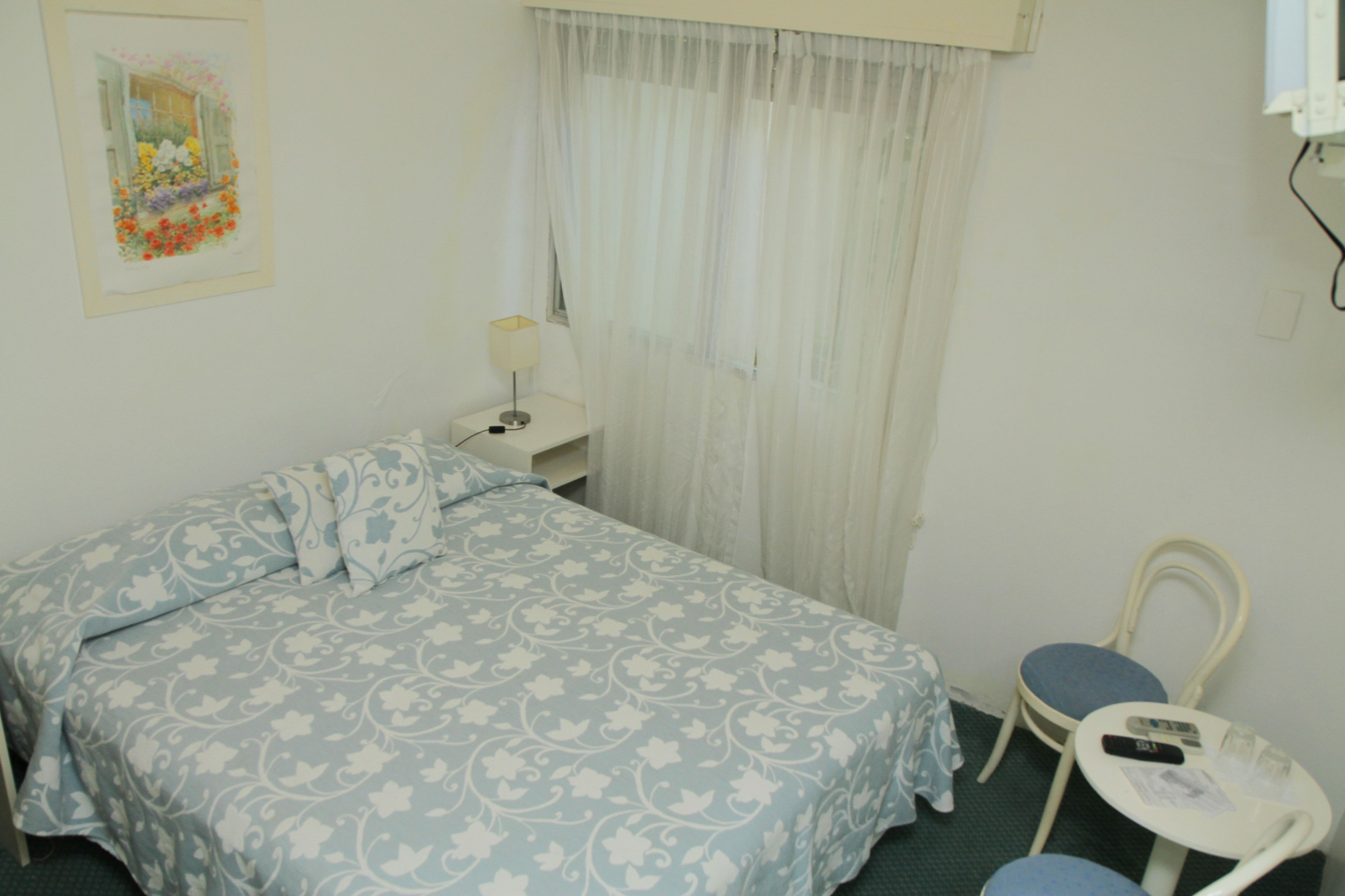 A bedroom with a bed, a chair, a nightstand, and a window with curtains.