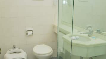 Un baño con inodoro, bidé y ducha con mampara de vidrio.