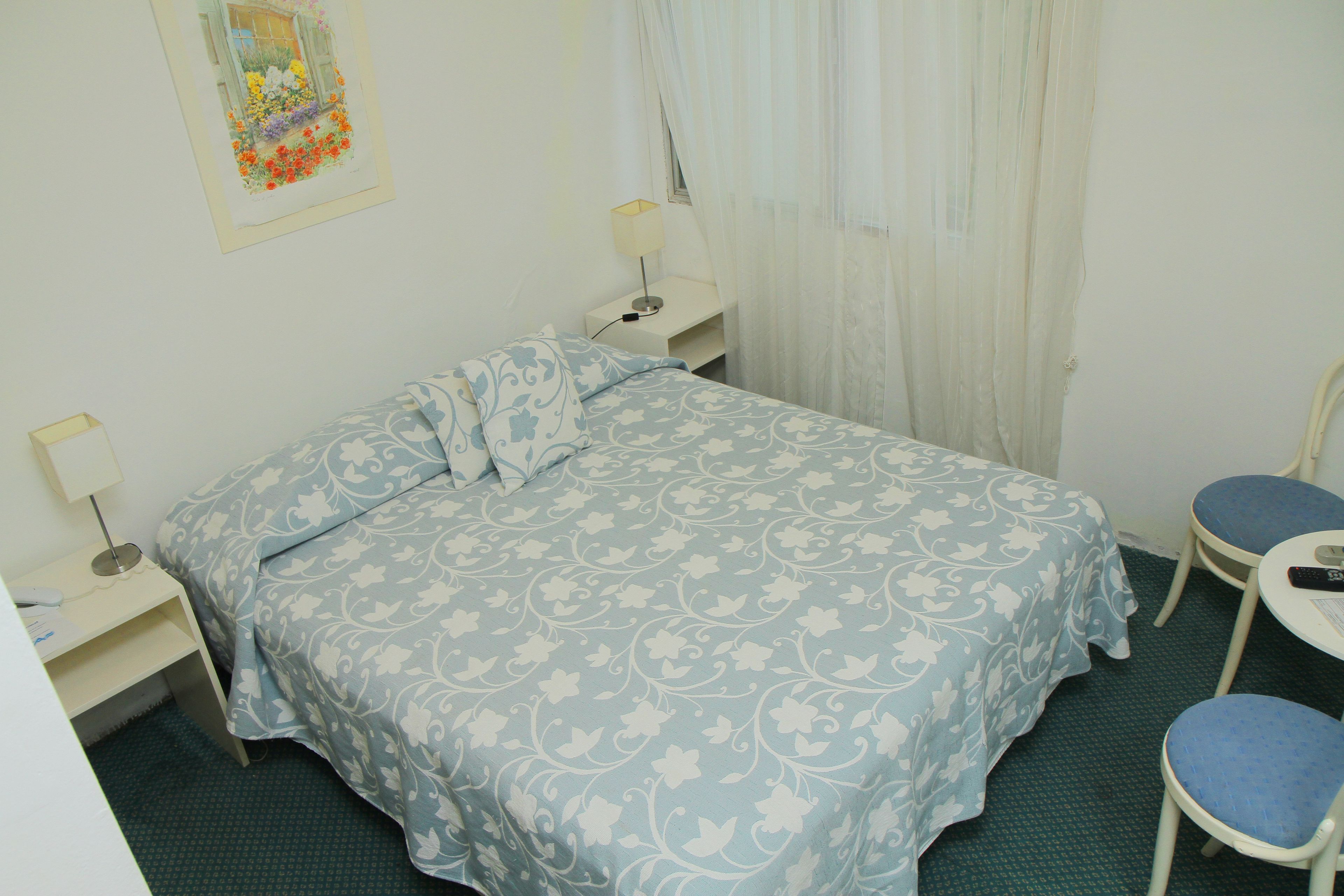 Un dormitorio con una cama, dos mesitas de noche, una silla y una pequeña mesa.