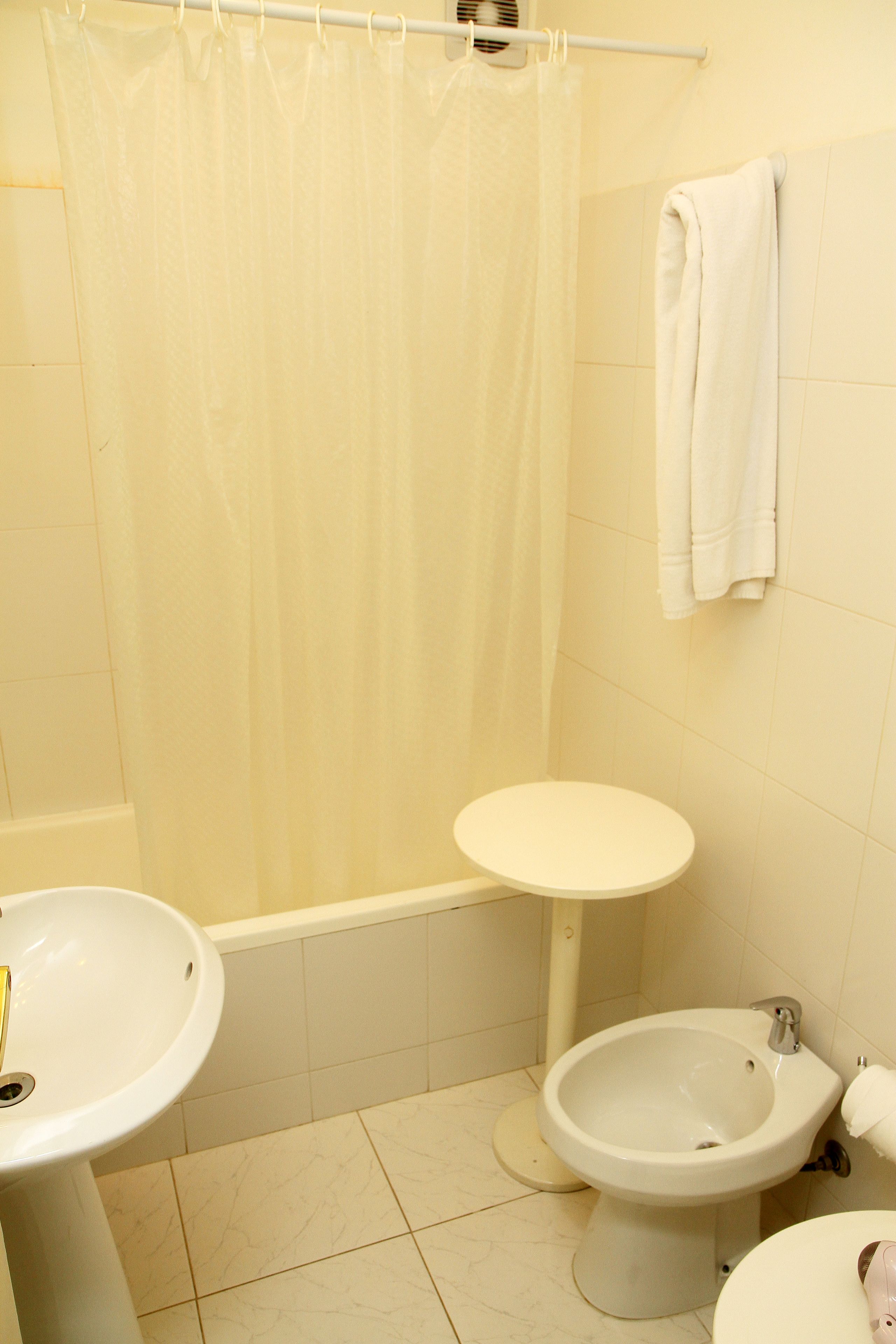 A bathroom with a shower curtain, a sink, a toilet, and a bidet.