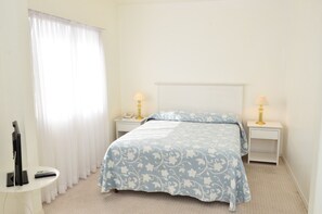 A bedroom with a bed, two bedside tables with lamps, a TV, and a window with curtains. - Hotel Aqua (Punta del Este)