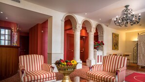 A lobby with striped armchairs, a glass coffee table, a fruit bowl, and a chandelier.
