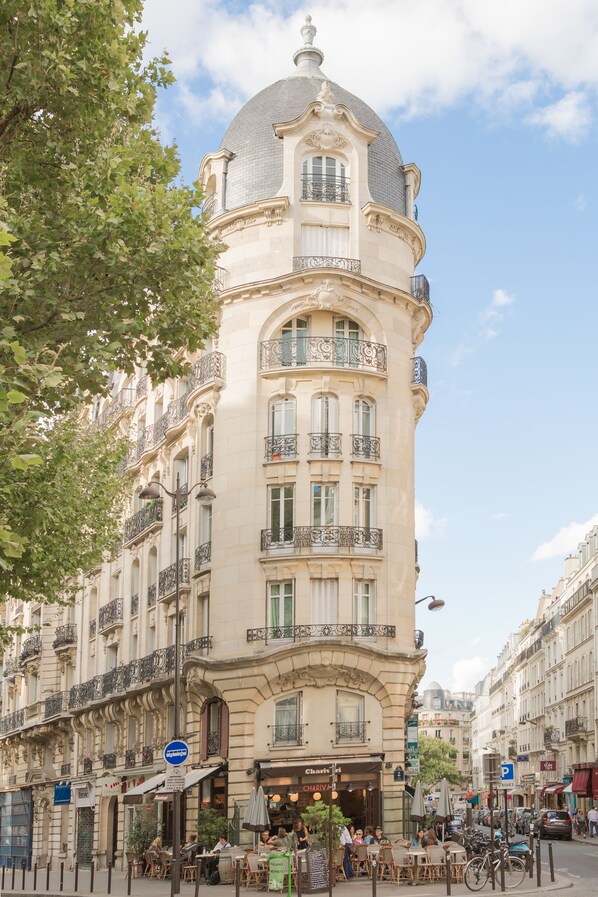 A historic building with a dome and ornate balconies, featuring outdoor seating and a café on the ground floor.