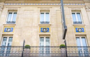 Un edificio con tres ventanas, cada una adornada con un arreglo decorativo y un balcón con barandilla de hierro forjado.