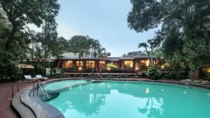 A swimming pool with a stone edge, surrounded by lush greenery and a building with multiple windows and lights. - Club Mahindra Thekkady (Peermade)