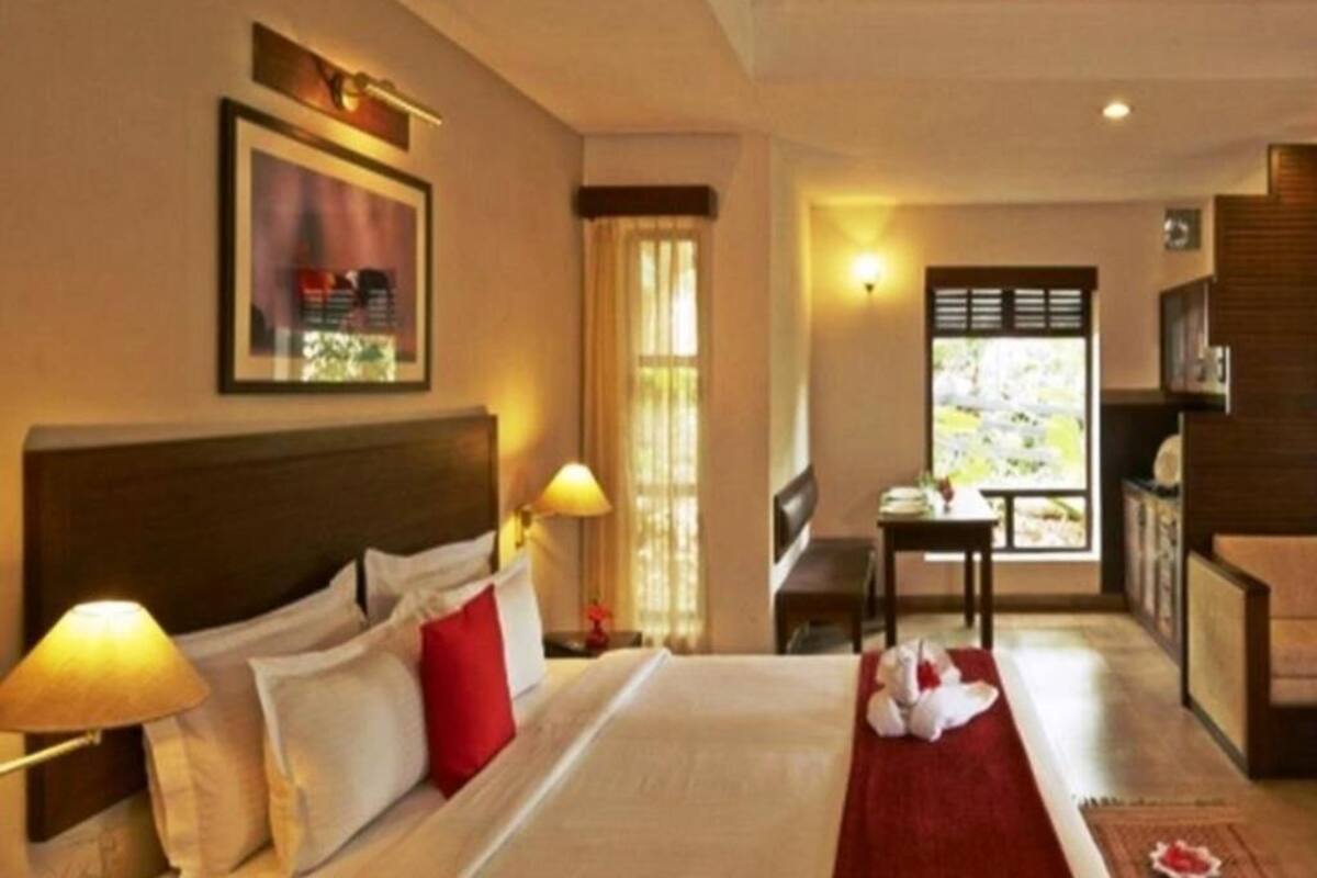 A hotel room with a bed, a desk, a chair, a window with a view, and a painting on the wall.