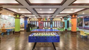 Relax in a vibrant space with a foosball table, surrounded by green chairs and tables, and colorful murals.