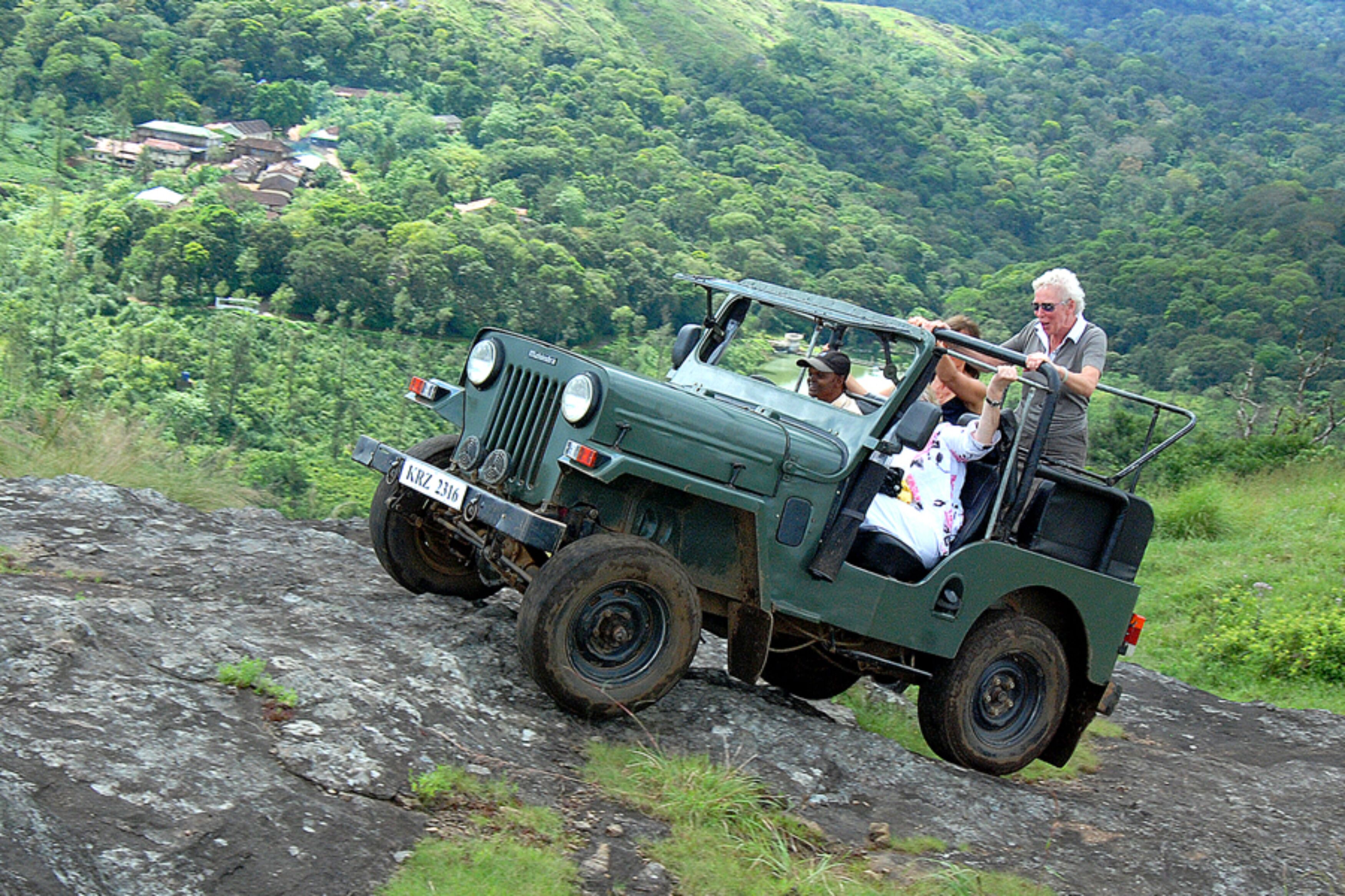 A green off-road vehicle with passengers on a rocky path surrounded by lush greenery.