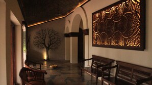 Un pasillo con bancos de madera, una pared con elaborados diseños tallados y un mural de un árbol.