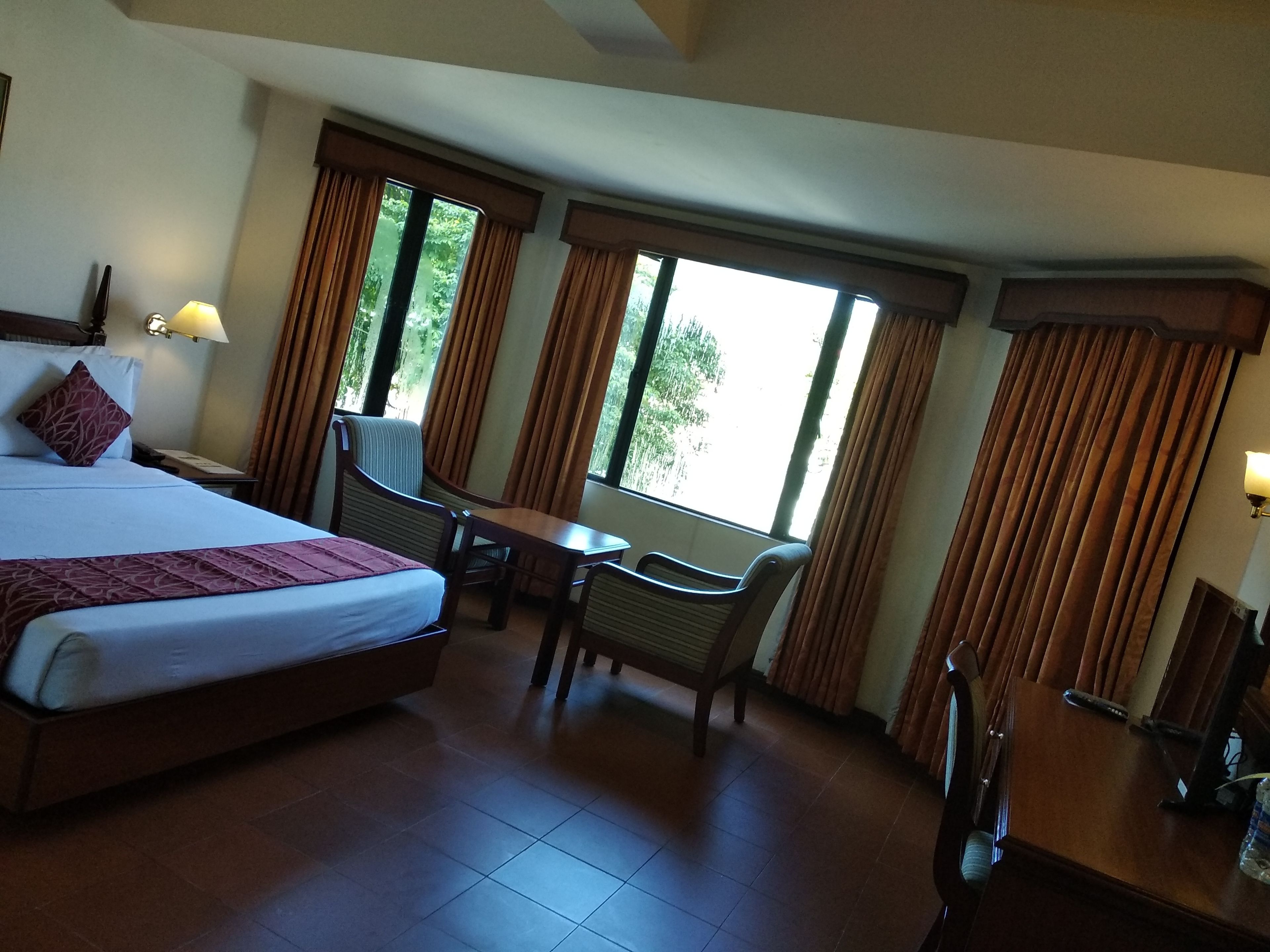 Una habitación de hotel con una cama grande, un escritorio, dos sillas y una ventana con cortinas.