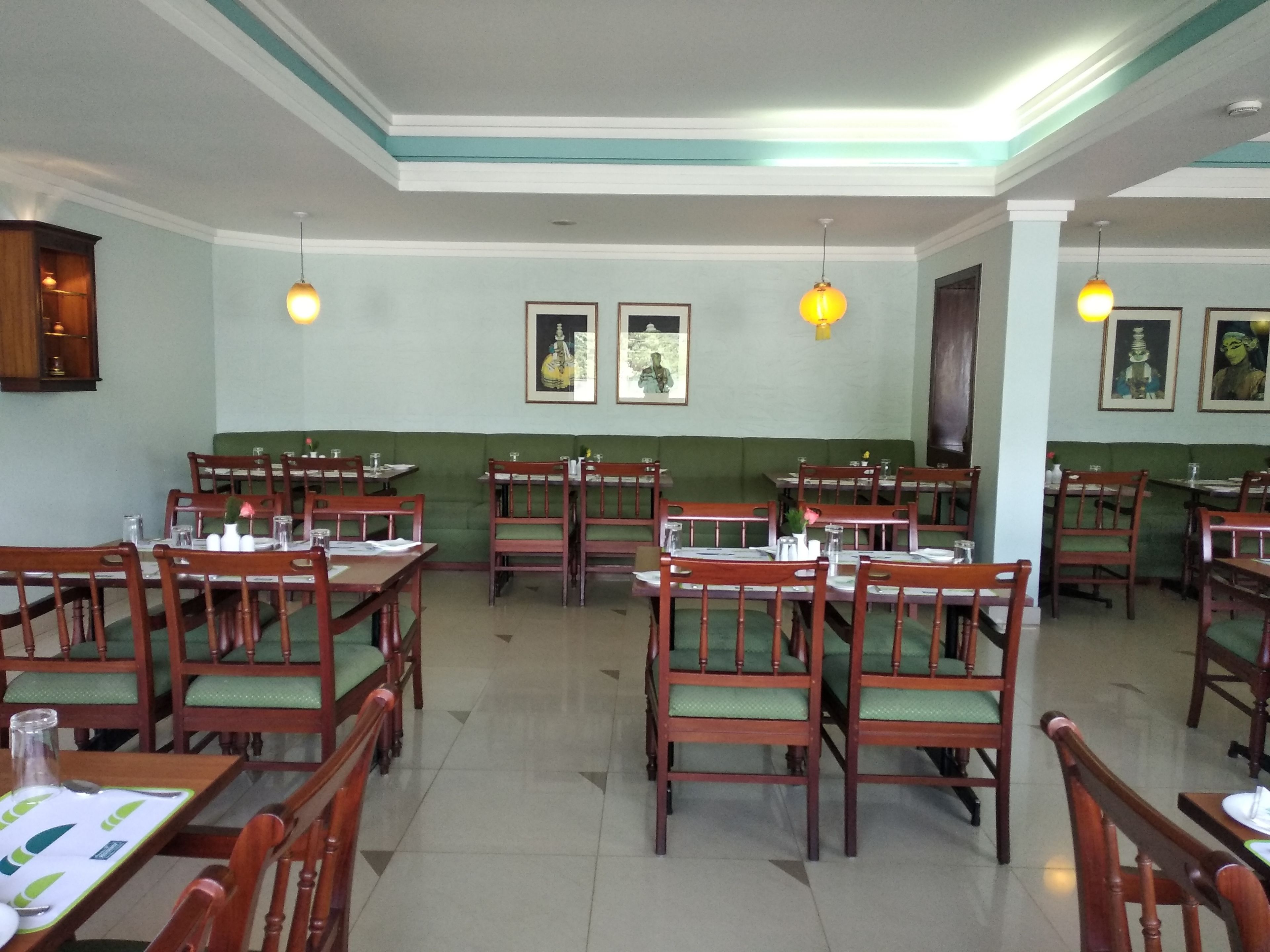 Un restaurant amb taules i cadires de fusta, seients amb coixinets verds i quadres a les parets.