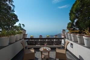 A terrace with wicker chairs, a table with a plate of food and drinks, potted plants, and a scenic view. - Fort Resorts Mussoorie (Dehradun)