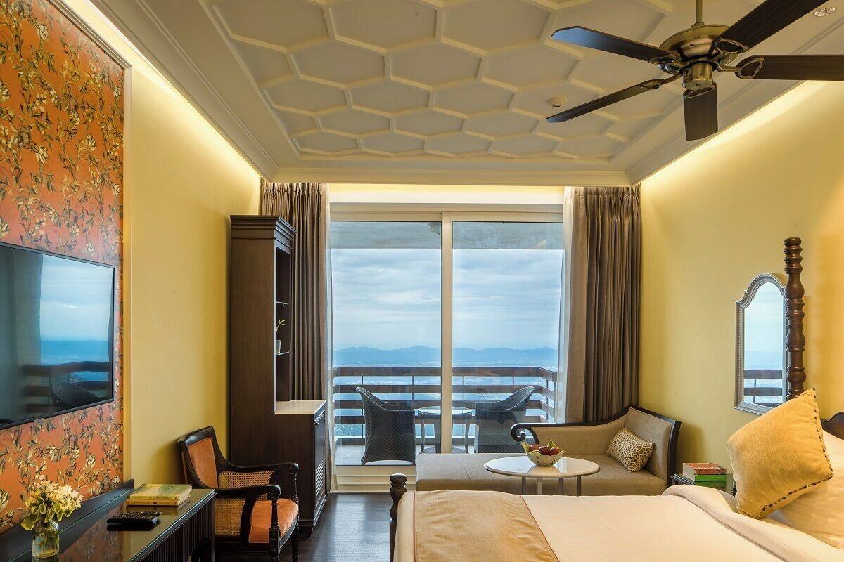 Une chambre d’hôtel équipée d’un lit, d’un bureau, d’une chaise, d’une petite table, d’une télévision et d’un balcon avec vue.