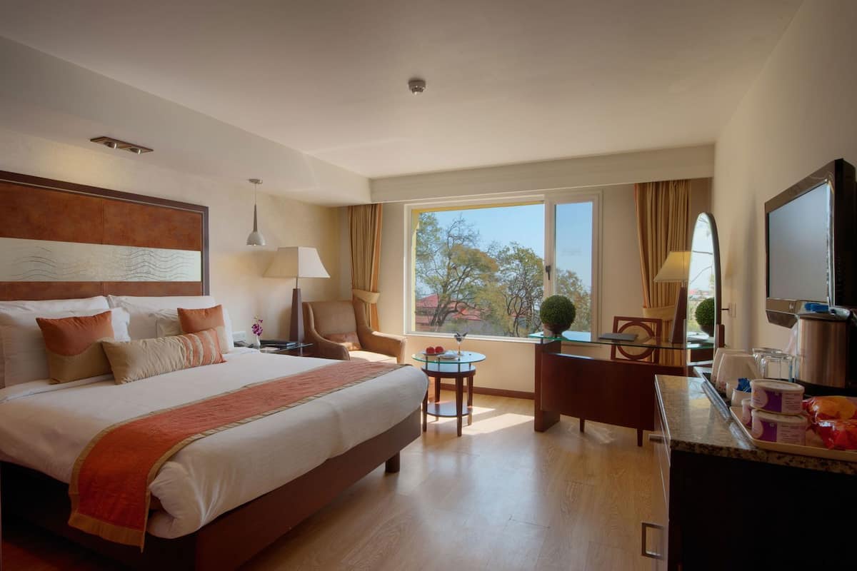 Une chambre d’hôtel avec un grand lit, un bureau, une chaise, une télévision et une fenêtre donnant sur un beau paysage.