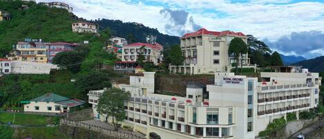 A multi-story hotel with a central courtyard, surrounded by lush greenery and hills.