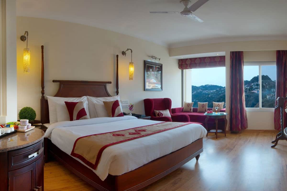 Une chambre d’hôtel avec un grand lit, un bureau, une chaise, une petite table et une vue sur le paysage.