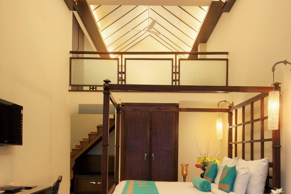 Une chambre à coucher avec un lit à baldaquin, un bureau, une chaise, un escalier et une lucarne.