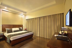 A hotel room with a large bed, wooden headboard, a flat-screen TV, a desk with a laptop, and a window with curtains. - Hotel Express Towers (Vadodara)