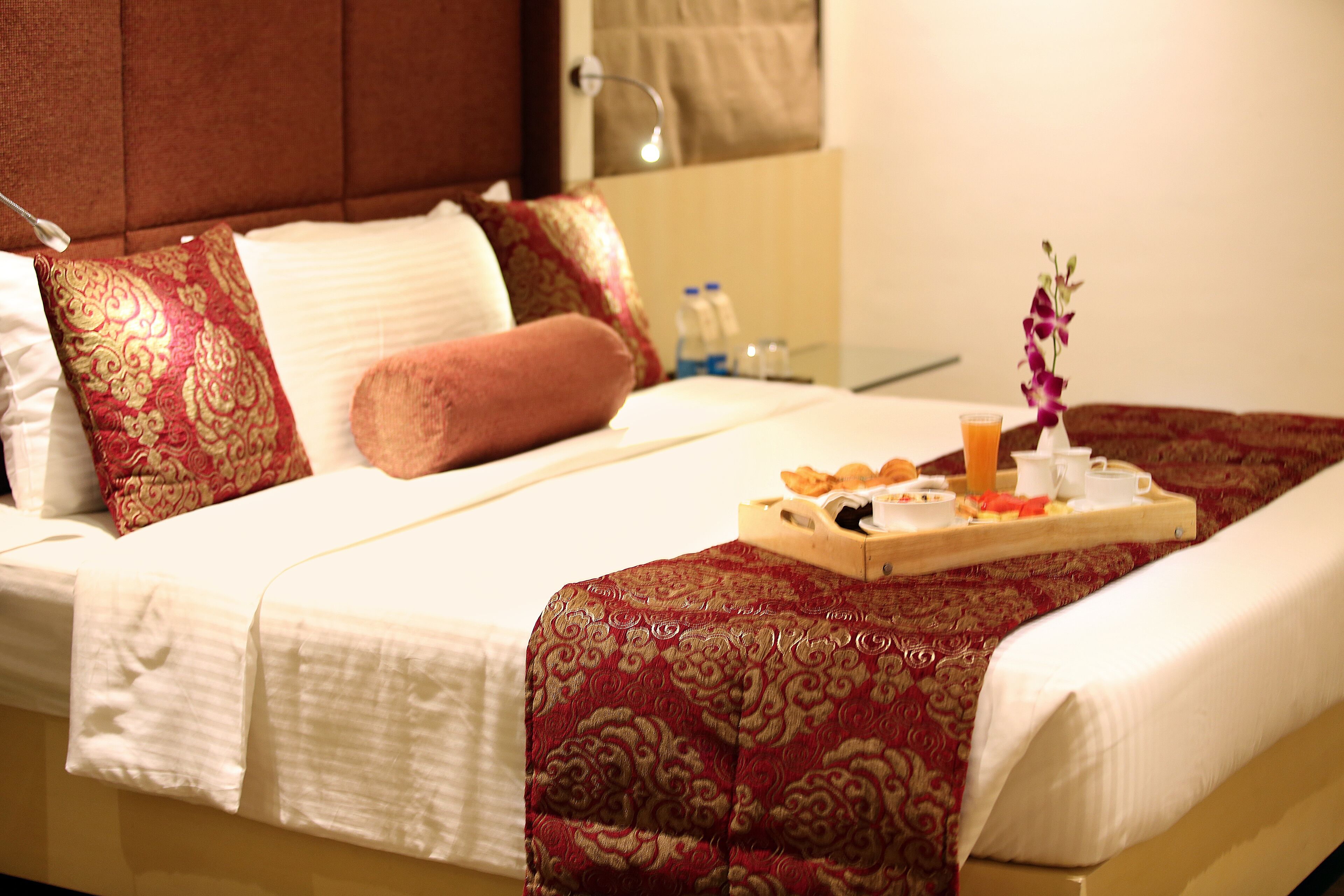 A neatly made bed with a tray of breakfast items, including orange juice, a cup, and pastries.