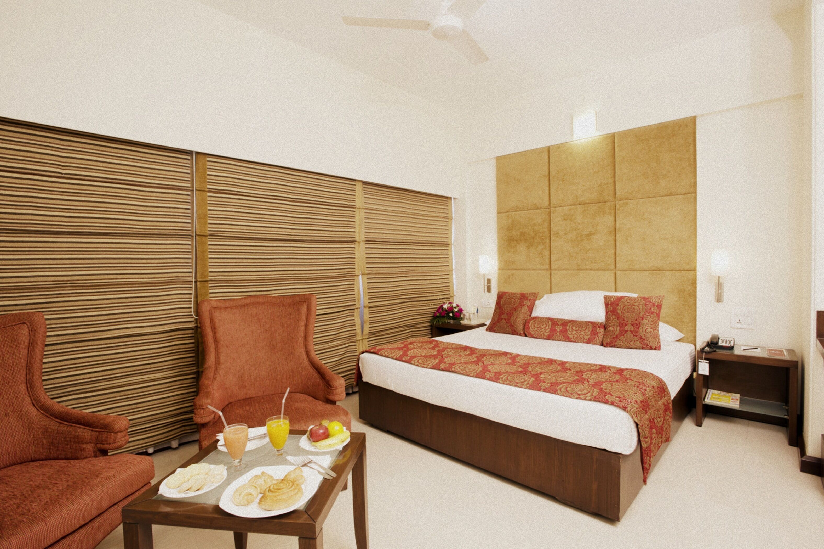 A hotel room with a bed, two armchairs, a table with breakfast, and a wooden partition wall.