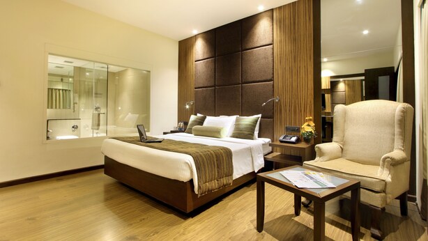 A modern hotel room with a large bed, a sitting area with a chair, a small table, and a large mirror. - Hotel Express Towers (Vadodara)