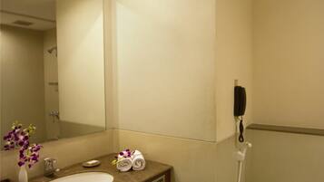 Un baño con lavamanos, espejo, inodoro y un teléfono colocado en la pared.