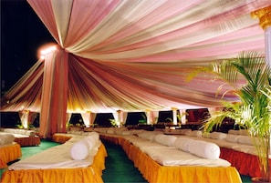 A tented outdoor event space with rows of beds, each with a white pillow and yellow skirt. - Hotel Express Towers (Vadodara)