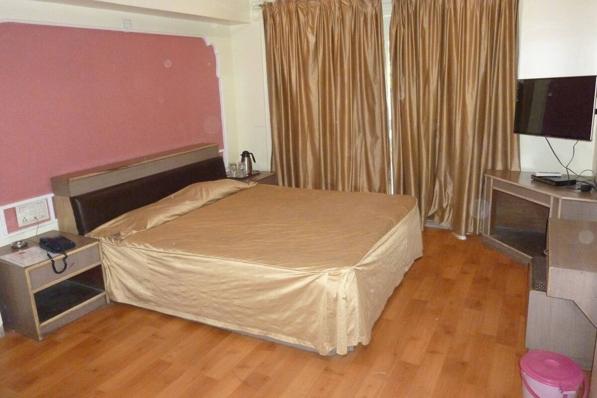 A hotel room with a large bed, a desk with a computer, a TV, and curtains.