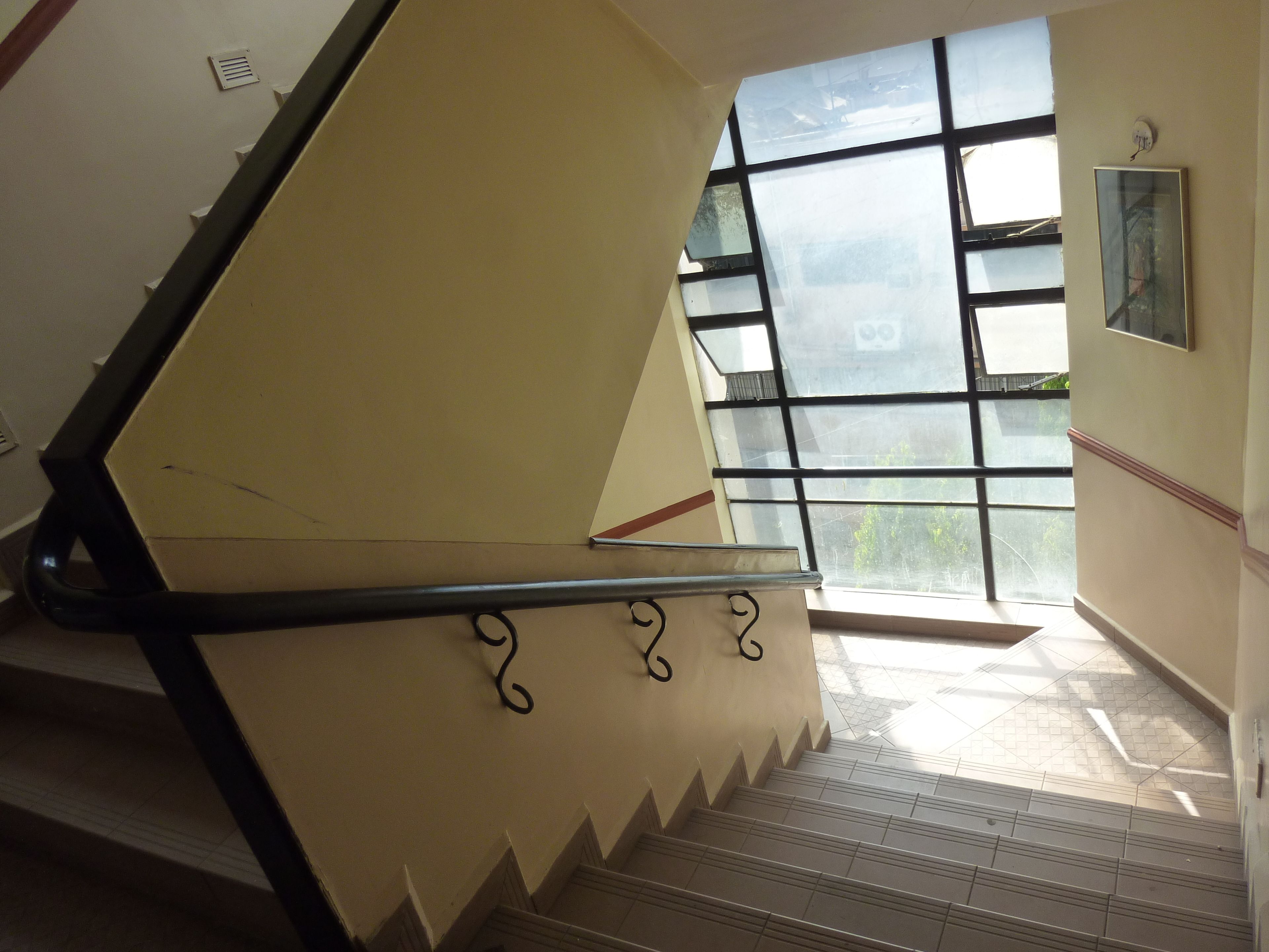 Un escalier muni d’une rampe et une fenêtre donnant sur un paysage verdoyant.