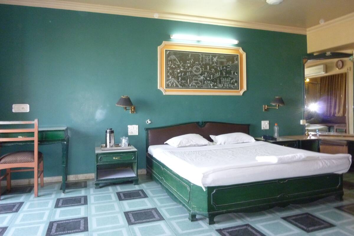 A hotel room with a bed, bedside tables, a chair, a mirror, and a wall-mounted picture.