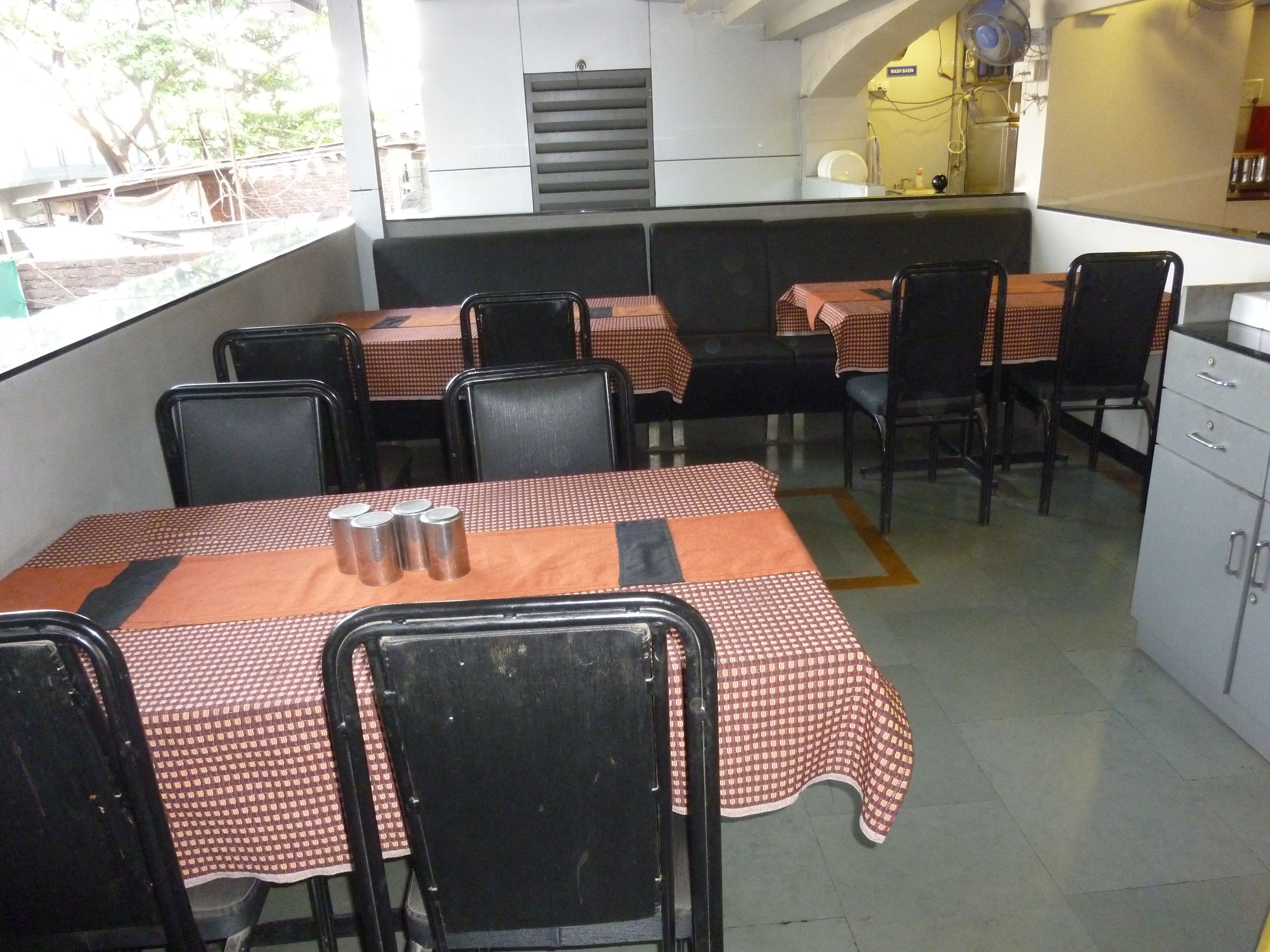 Un coin repas avec des tables recouvertes de nappes à carreaux, des chaises noires et un réfrigérateur en arrière-plan.