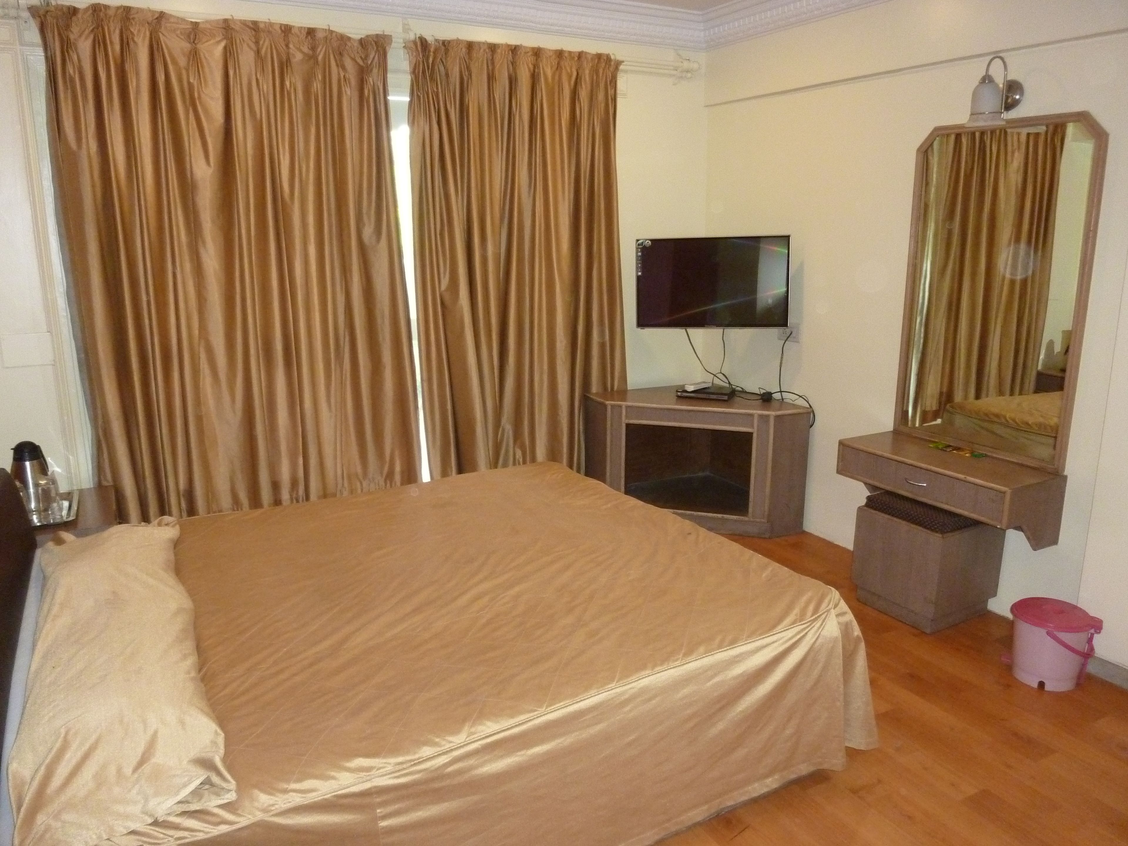 A hotel room with a large bed, a TV on a stand, a mirror above a vanity, and a trash bin.