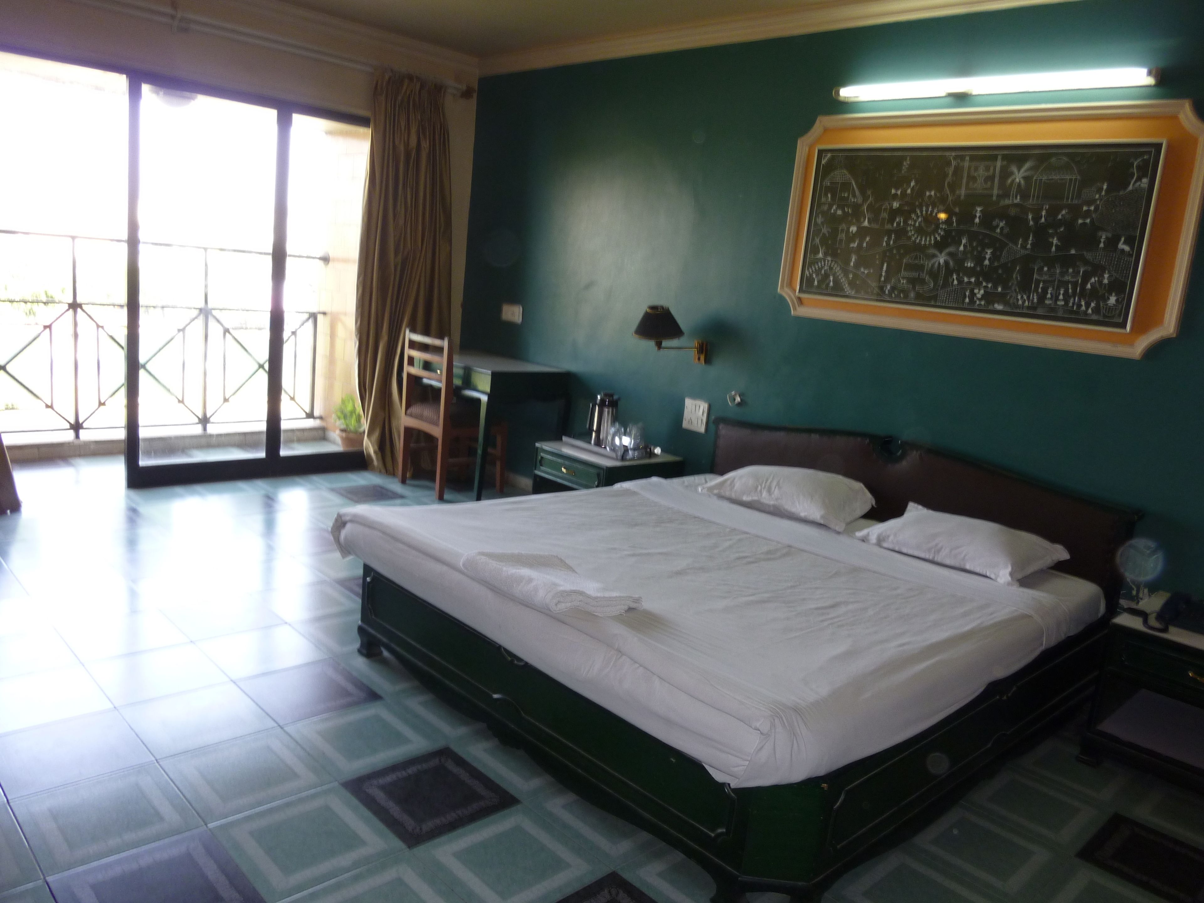 Ein Hotelzimmer mit einem großen Bett, einem Schreibtisch, einem Sessel und Blick durch die Glasdoor.