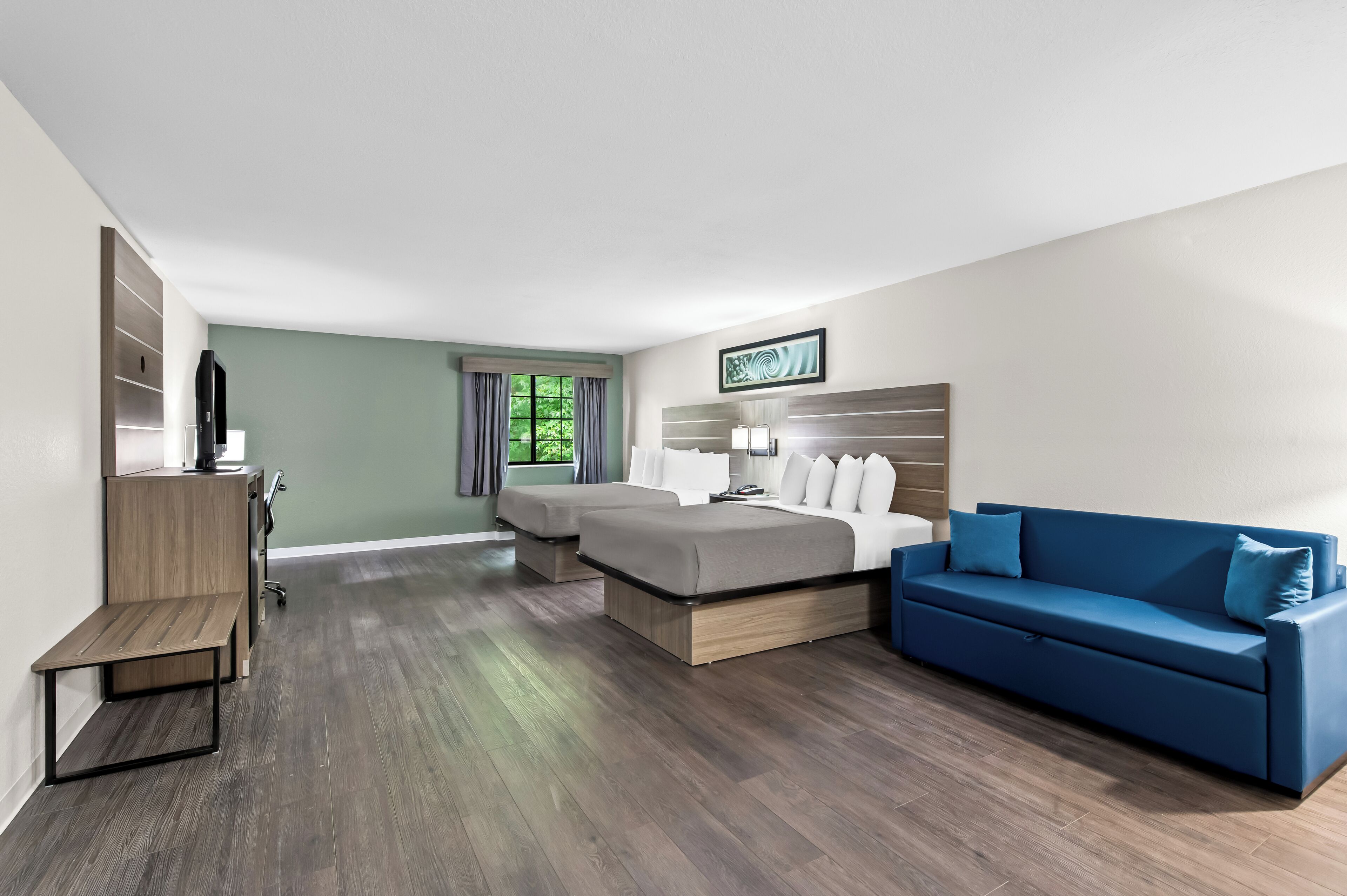 A modern hotel room with a large bed, a blue sofa, a desk, and a window with curtains.
